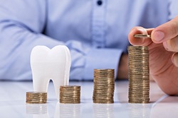 Person stacking coins next to a tooth