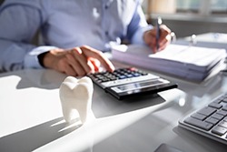 Person at a desk with a calculator and model tooth.