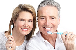 An older couple smiling and holding toothbrushes.