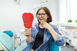 A woman staring at her smile in the mirror at the dentist office