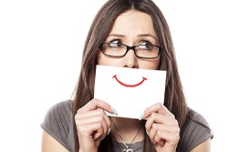 A woman holding up a sign with a fake smile drawn on it to cover her mouth