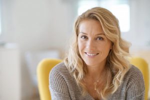 Woman smiling with porcelain veneers sitting in yellow chair