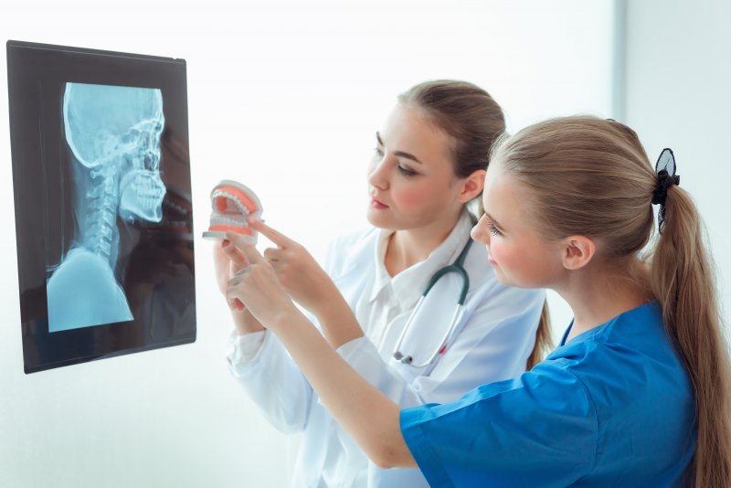 dentists looking at an x-ray and pointing at a model of teeth