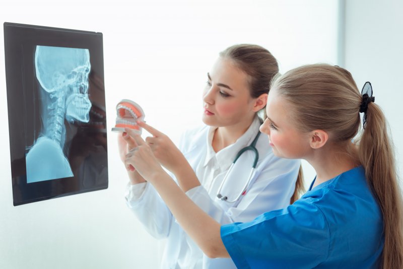 dentists looking at an x-ray and pointing at a model of teeth