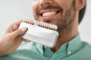 Hand holding up dental veneers to smiling young man.
